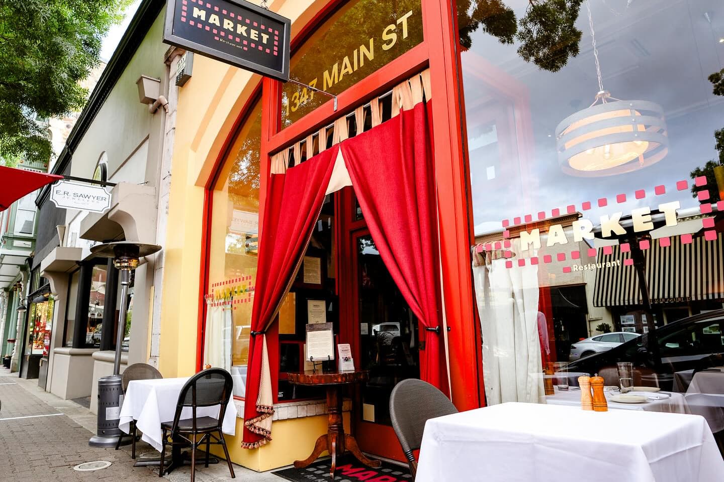 Restaurant storefront with red curtains and outdoor tables
