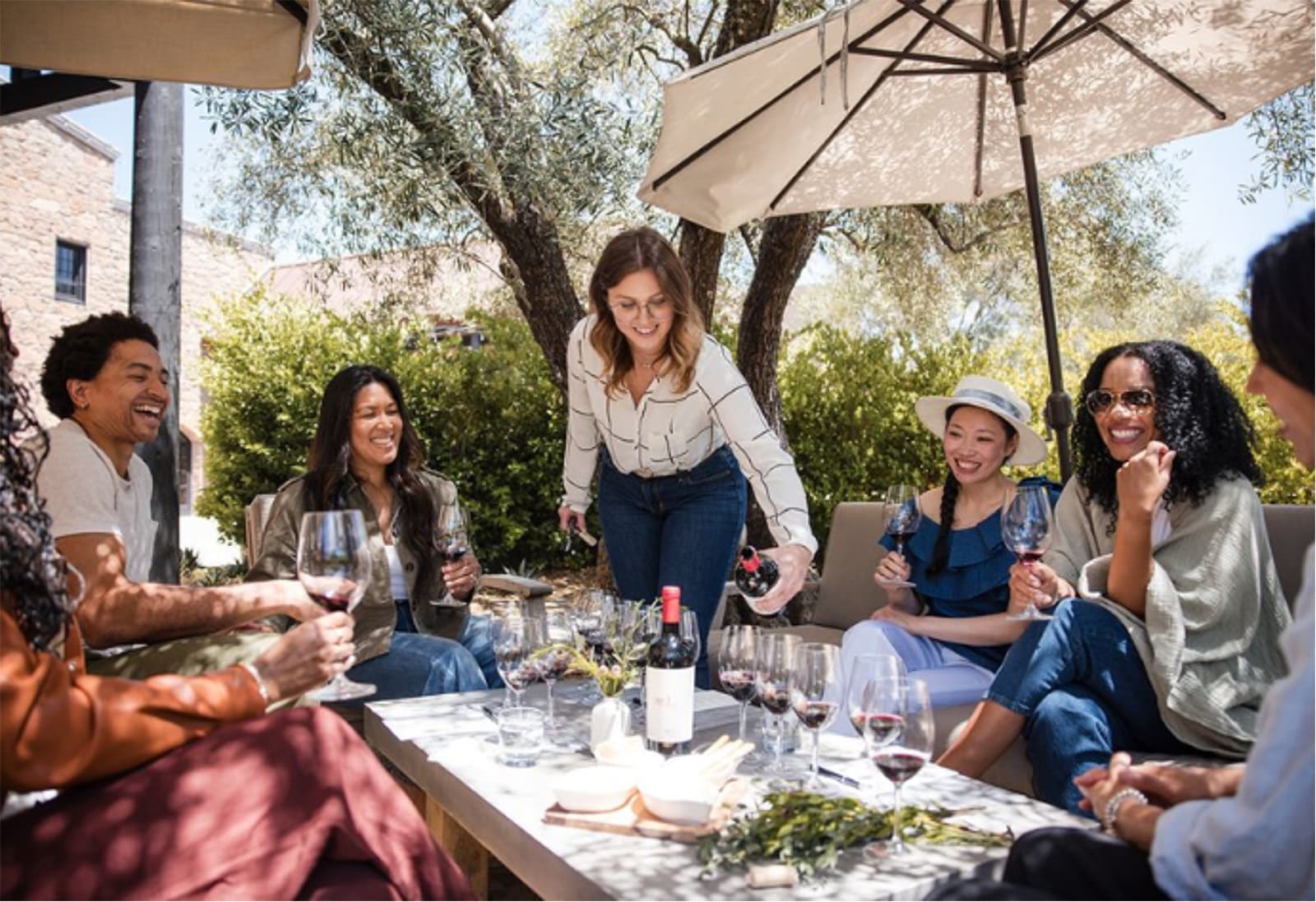 Friends enjoying wine outdoors under umbrella.