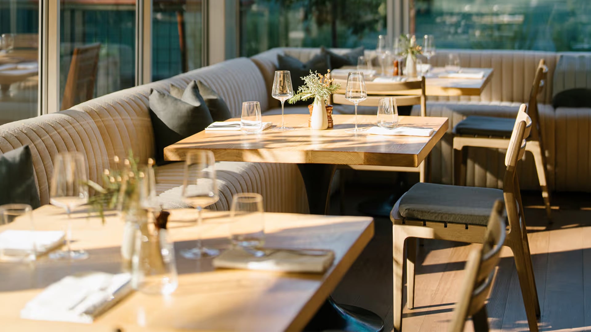 Sunlit restaurant tables with wine glasses and booth seating