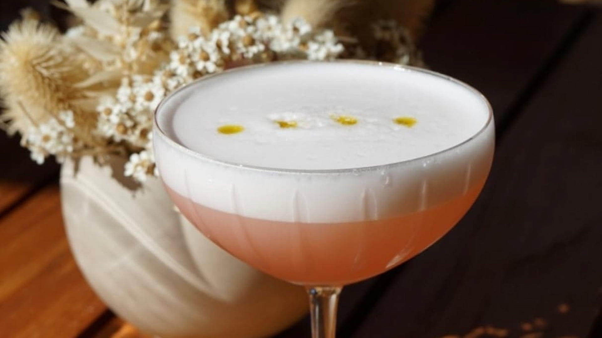 Elegant cocktail with frothy top and floral backdrop.