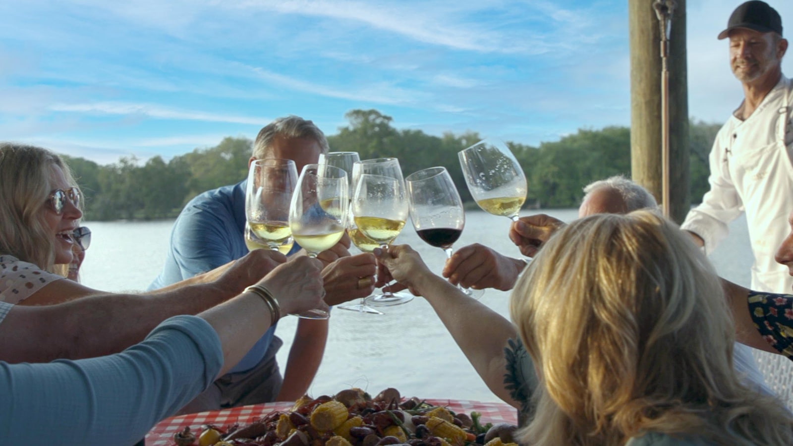Group toasting with wine outdoors by water