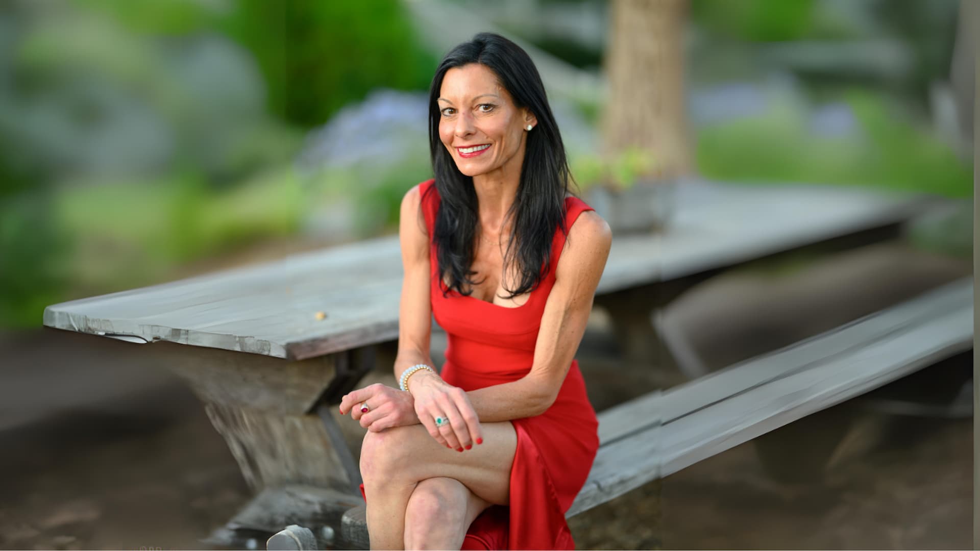 Woman in red dress sitting on bench outdoors.