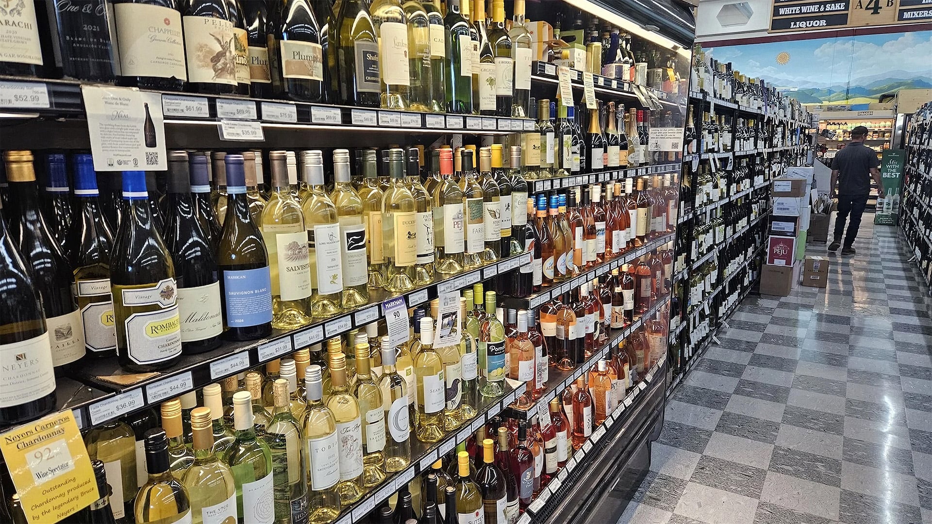 Wine bottles line shelves in a liquor store aisle.