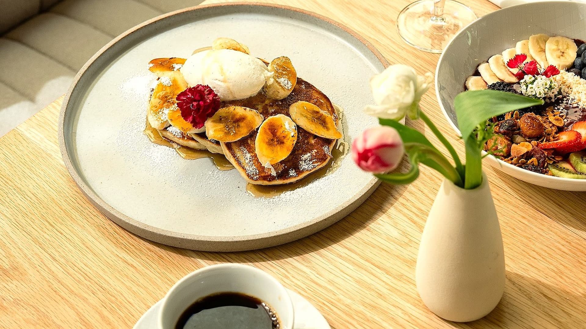 Pancakes with bananas and flowers on table