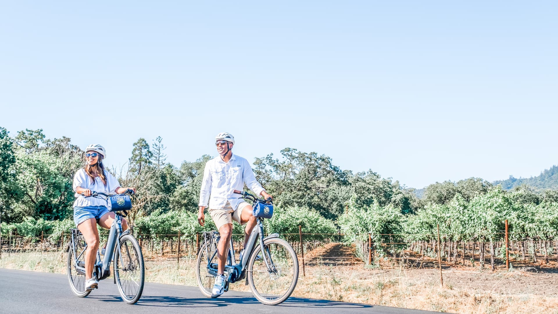 Couple biking through vineyard on a sunny day.