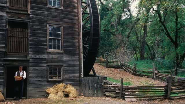 Historic watermill with wooden fences and trees.