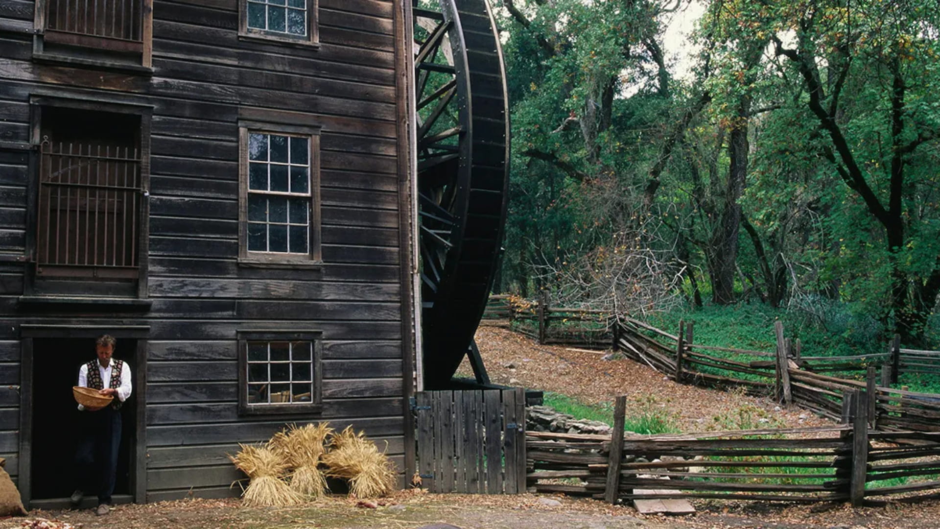 Historic watermill with wooden fences and trees.