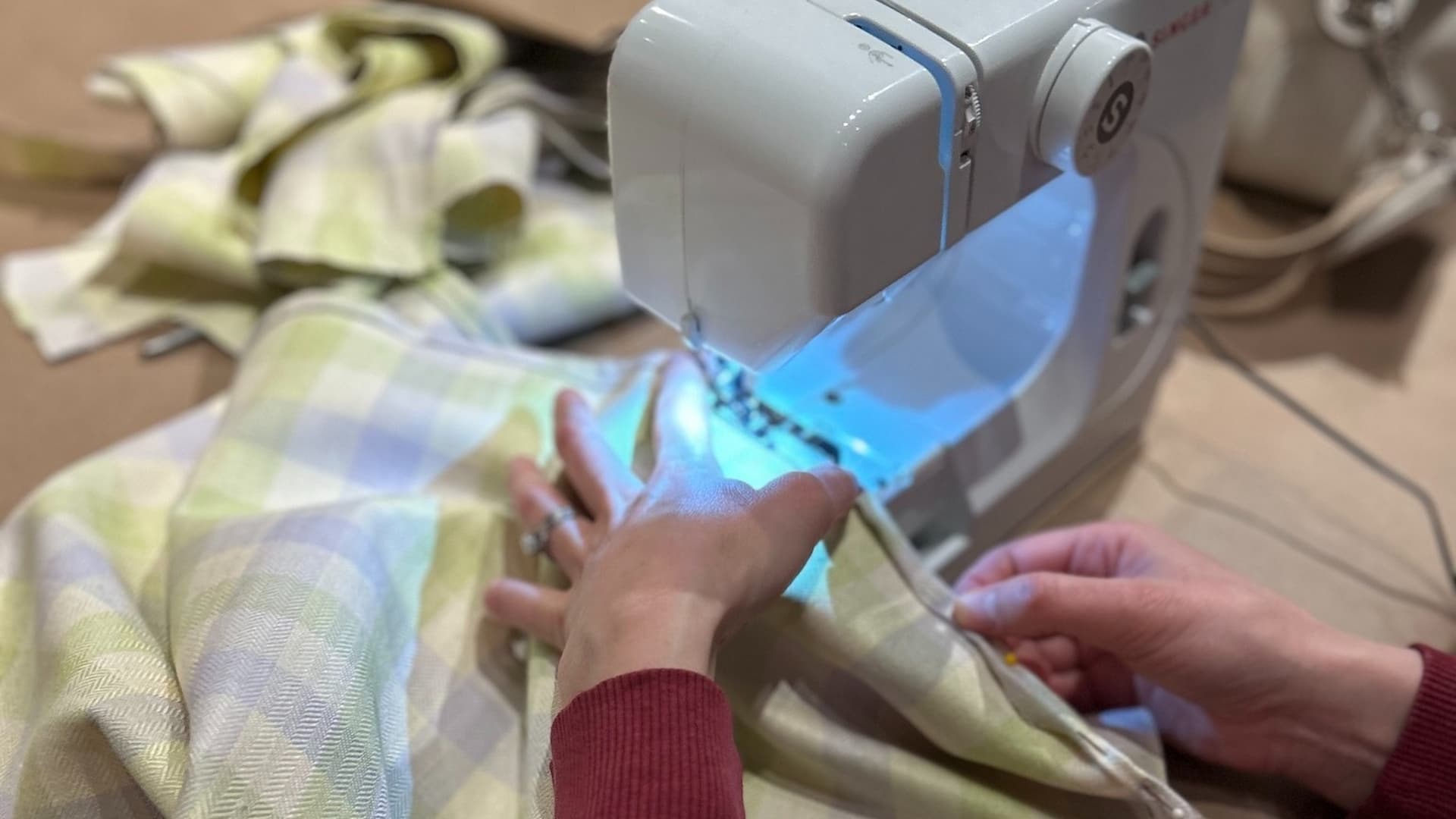 Hands sewing light-colored, checkered fabric with a white sewing machine
