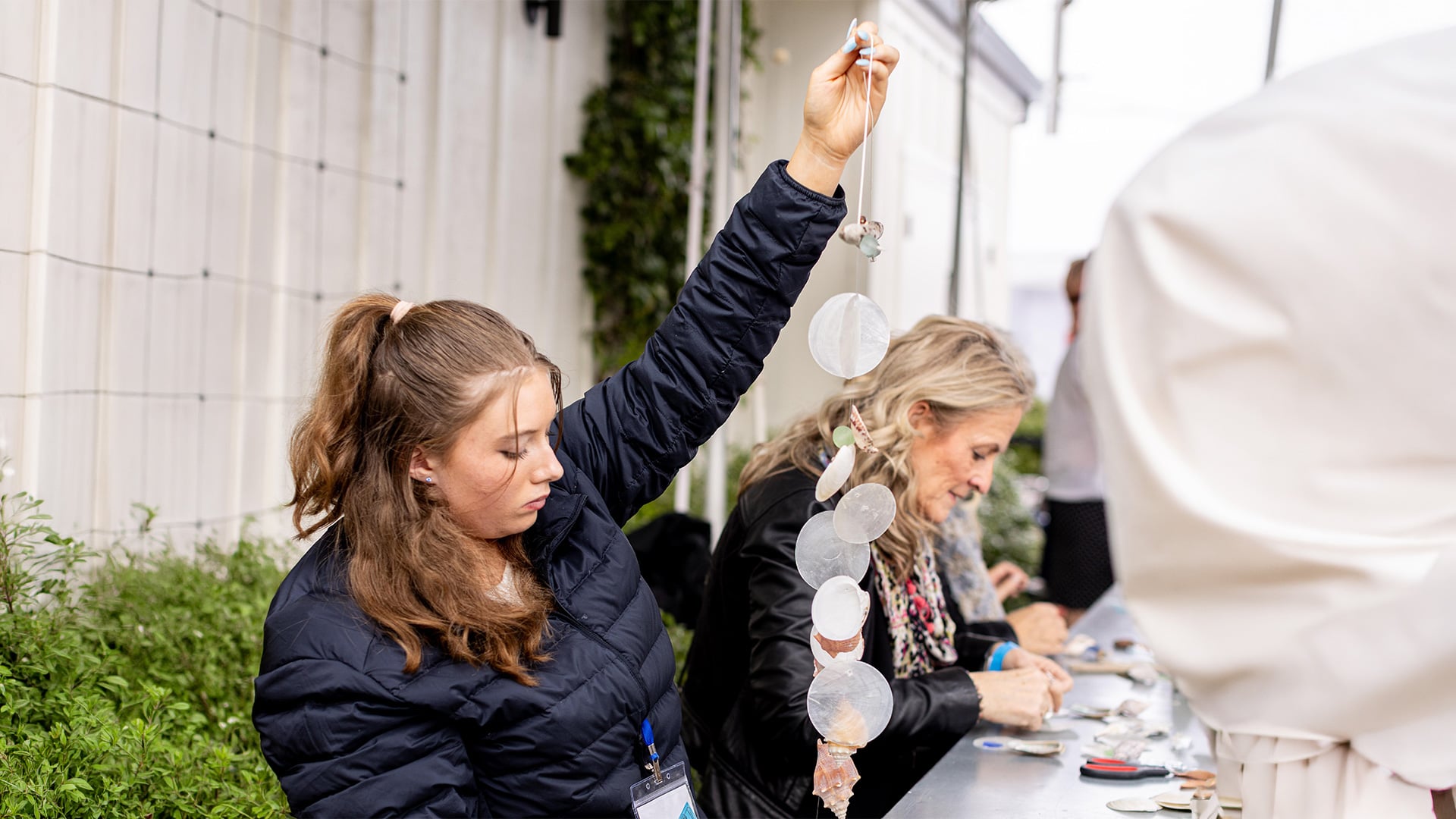 Woman holds handmade seashell mobile at outdoor craft table