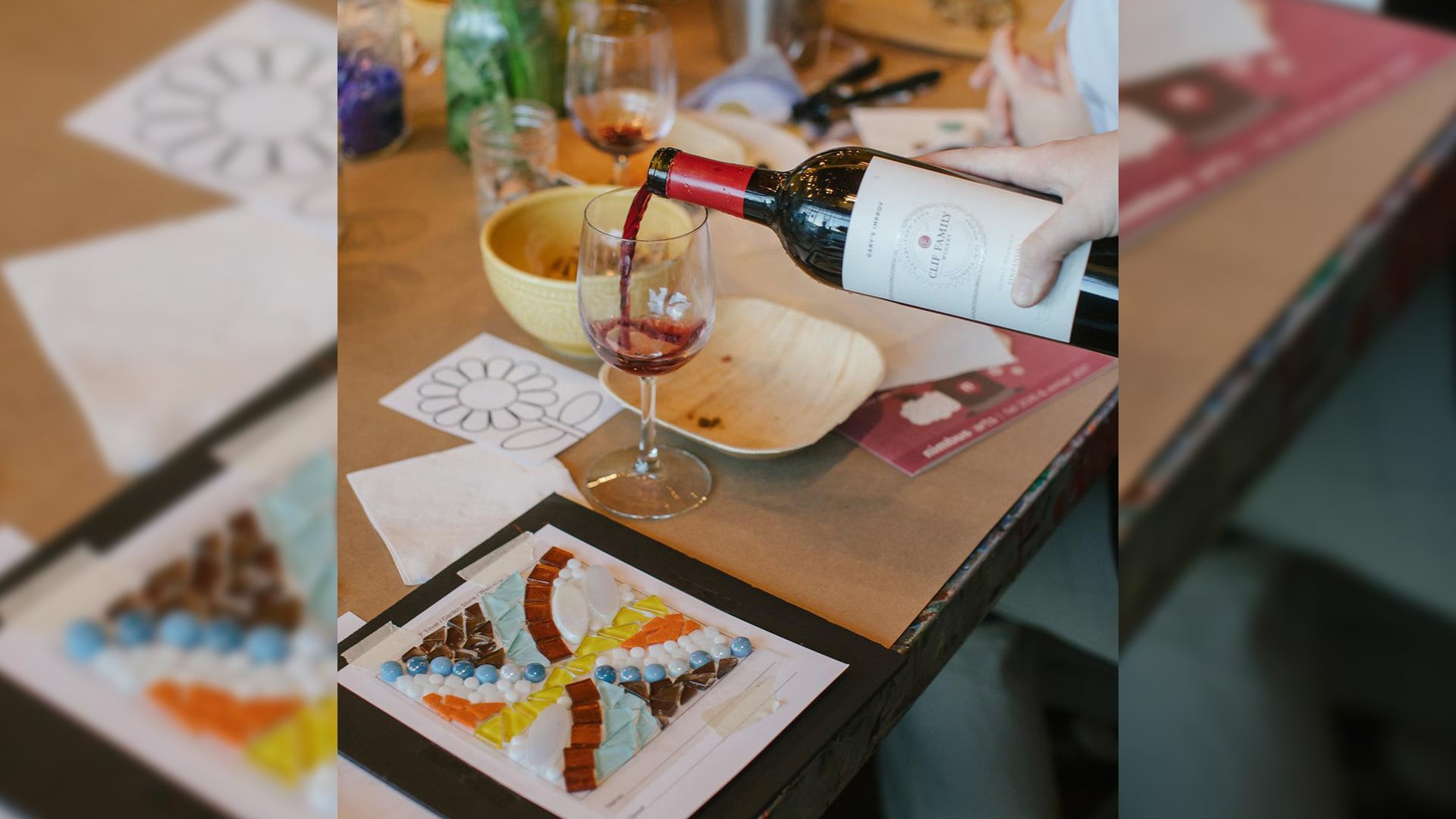 Person pours red wine beside colorful mosaic art