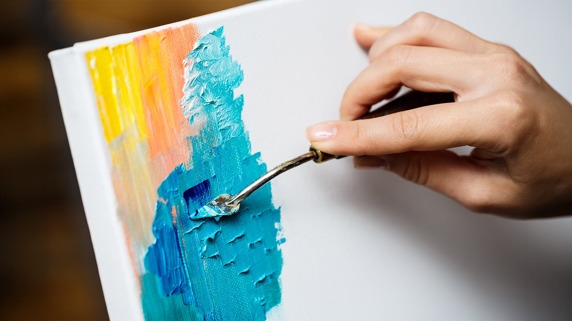 Artist applying turquoise paint to a canvas with palette knife