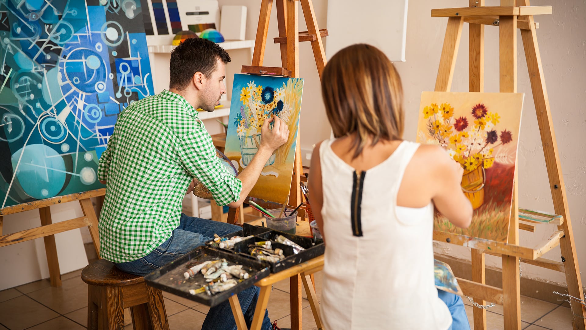 Two artists painting floral canvases in a studio