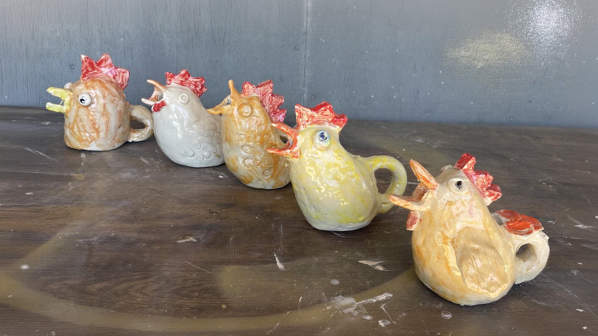 Five colorful ceramic rooster-shaped pitchers arranged on a tabletop