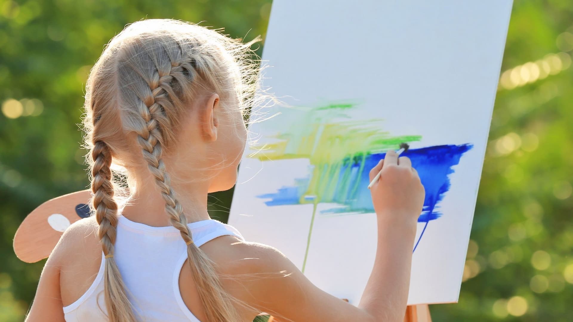 Girl with braids painting on outdoor canvas