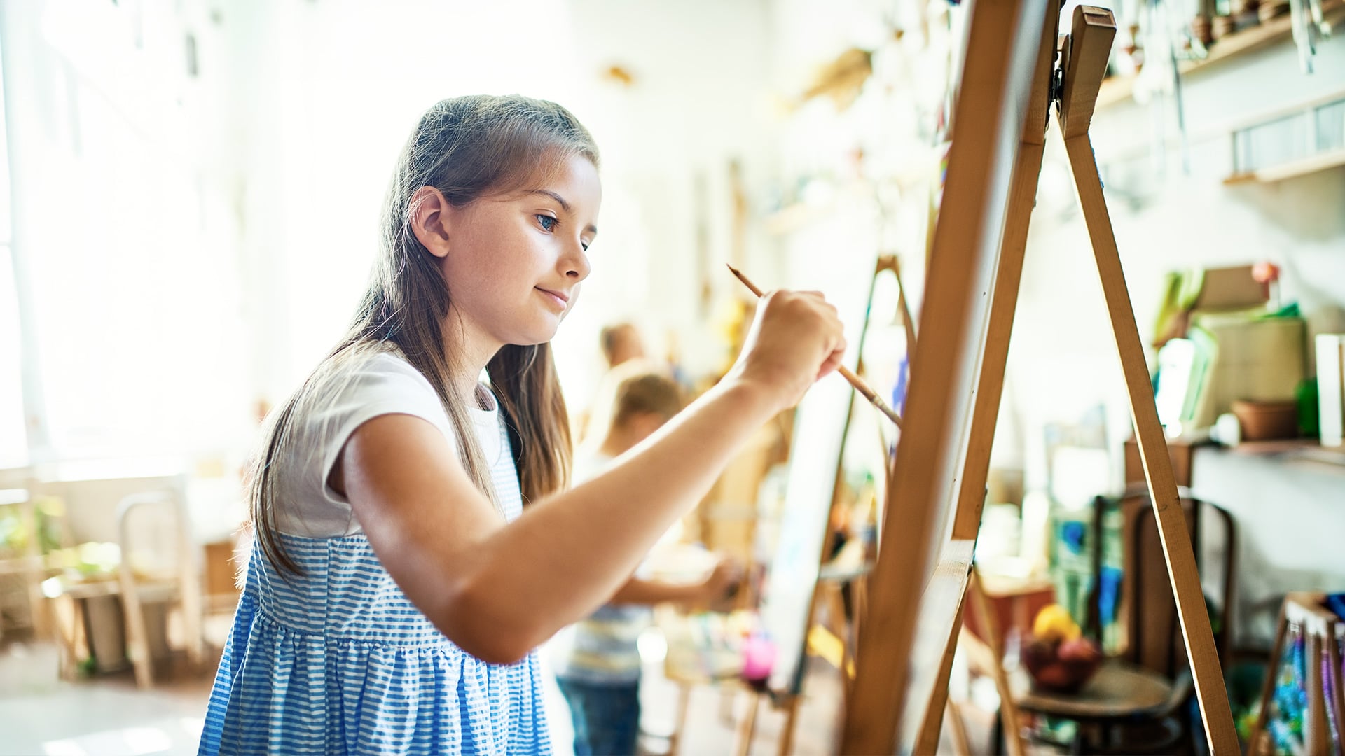 Young girl painting on an easel in art class