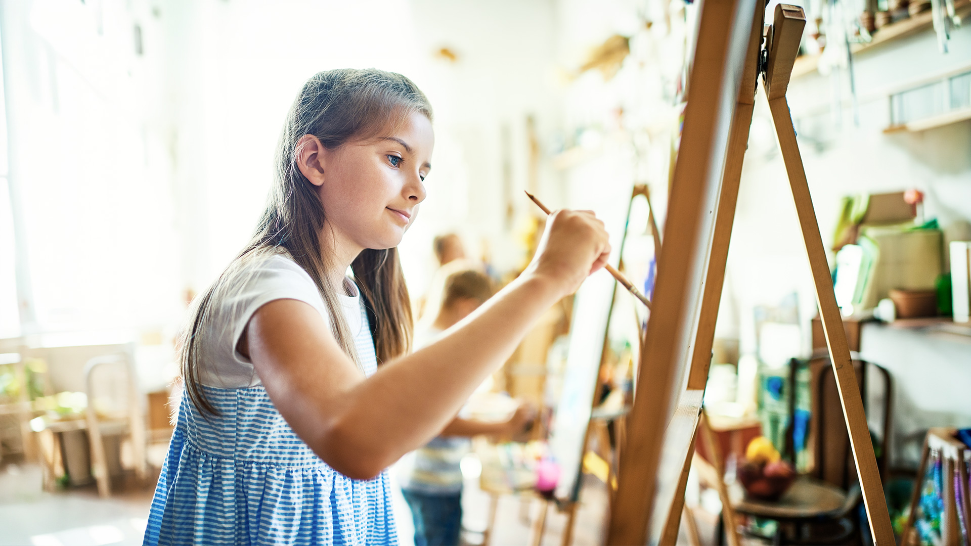 Young girl painting on an easel in art class