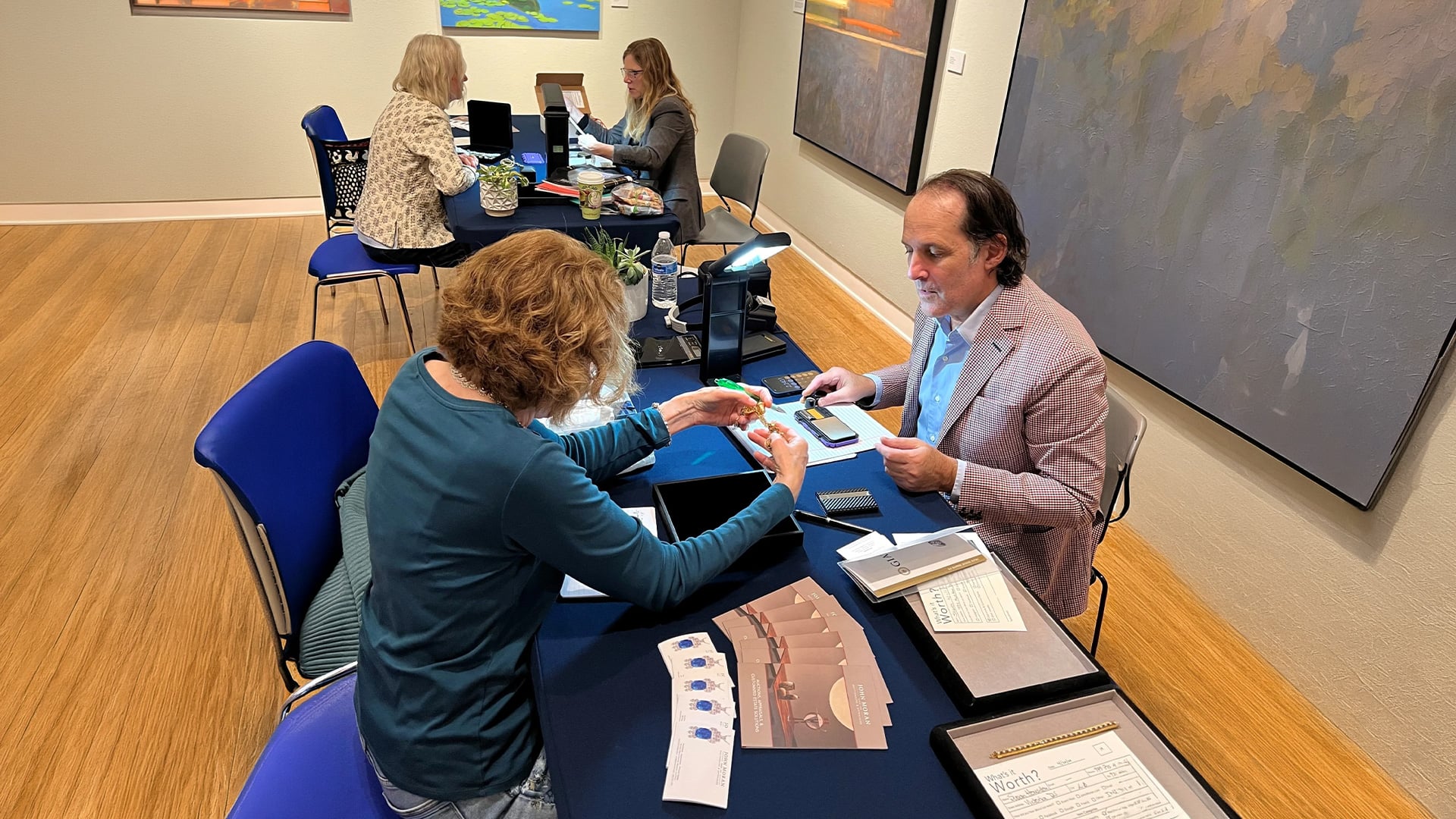 Expert appraisers examine items at tables in an art gallery.