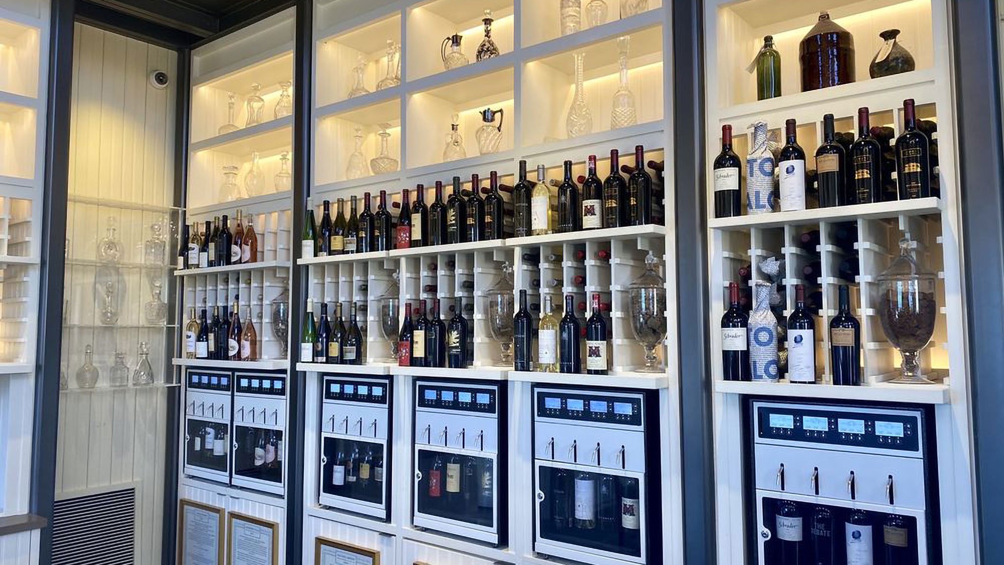 Wine bottles displayed on shelves with dispensers.
