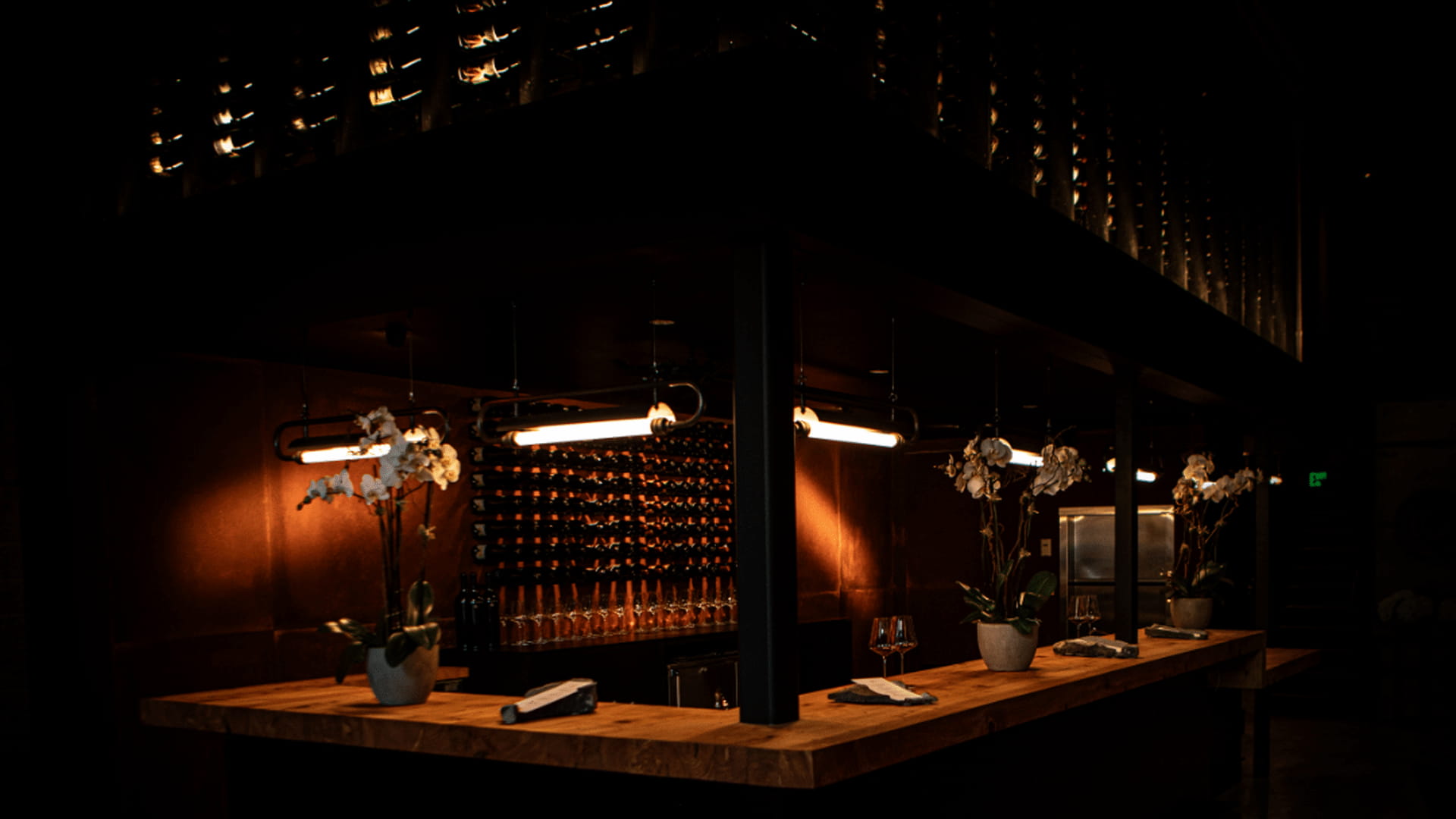 Dimly lit wine bar with wooden counter and flowers.