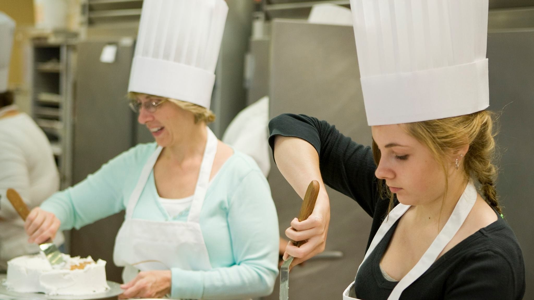 Bakers decorating cakes in a kitchen.