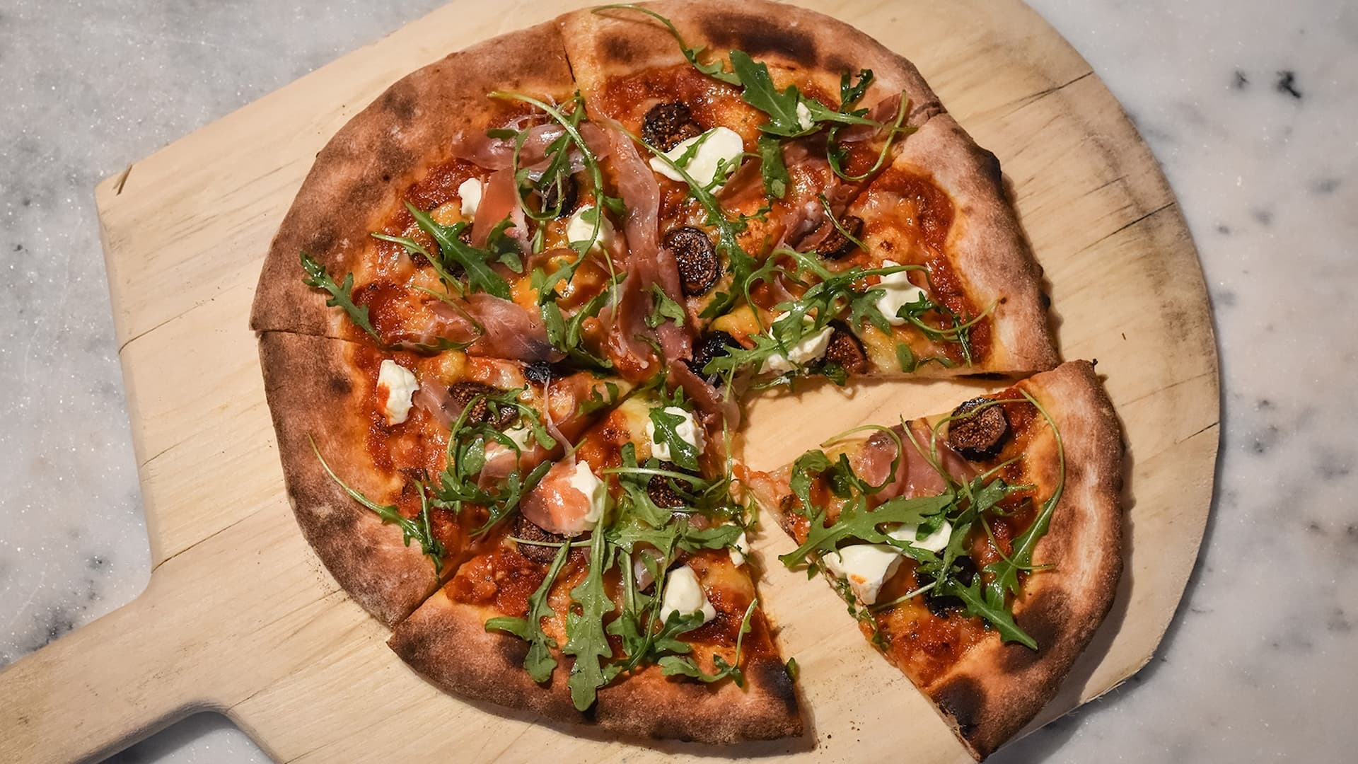Gourmet pizza with prosciutto and arugula on board.
