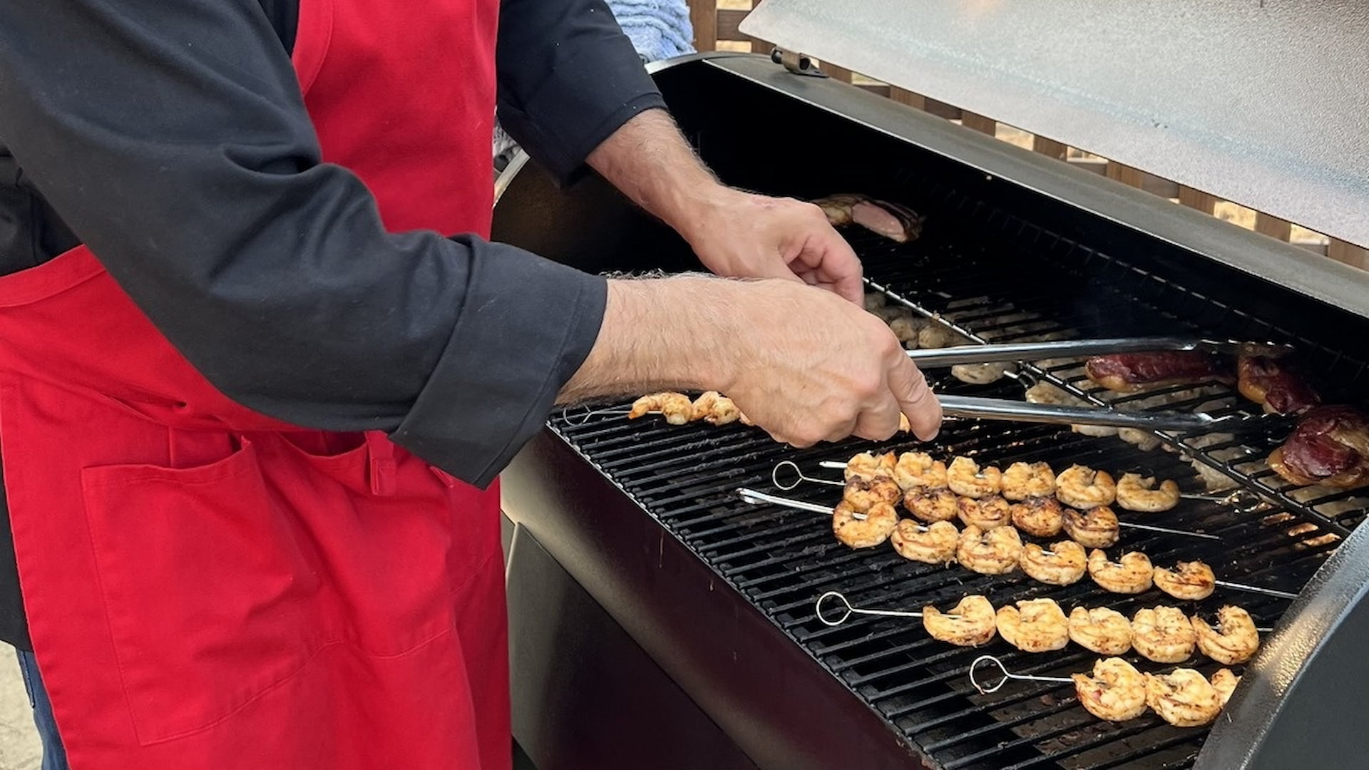 Person grilling shrimp skewers and meat.