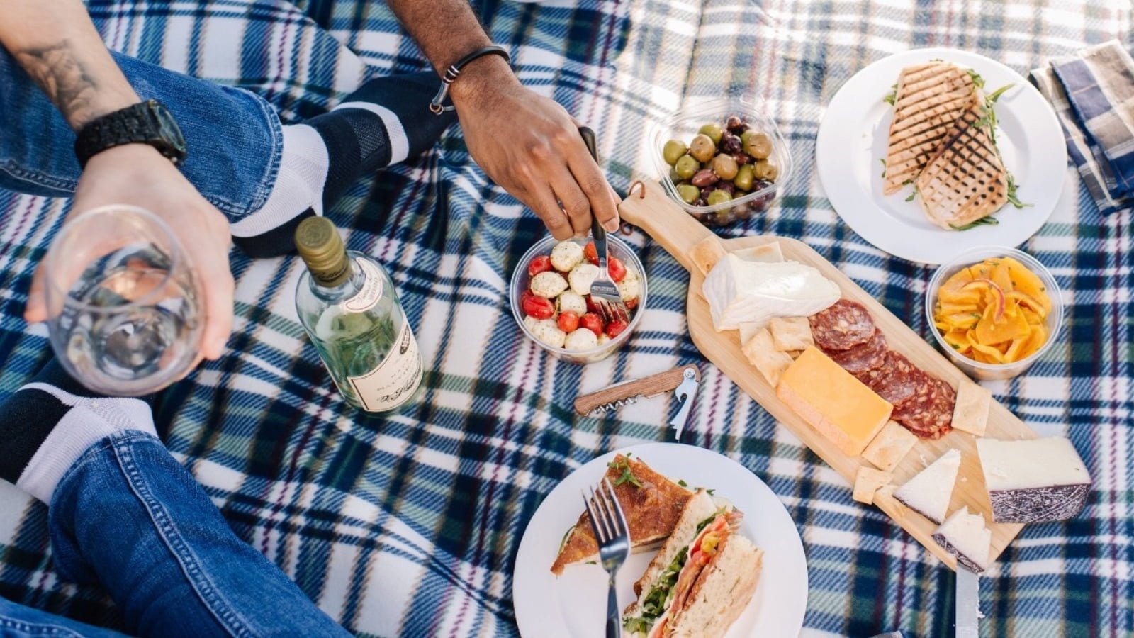 Outdoor picnic with sandwiches, cheese, and wine.