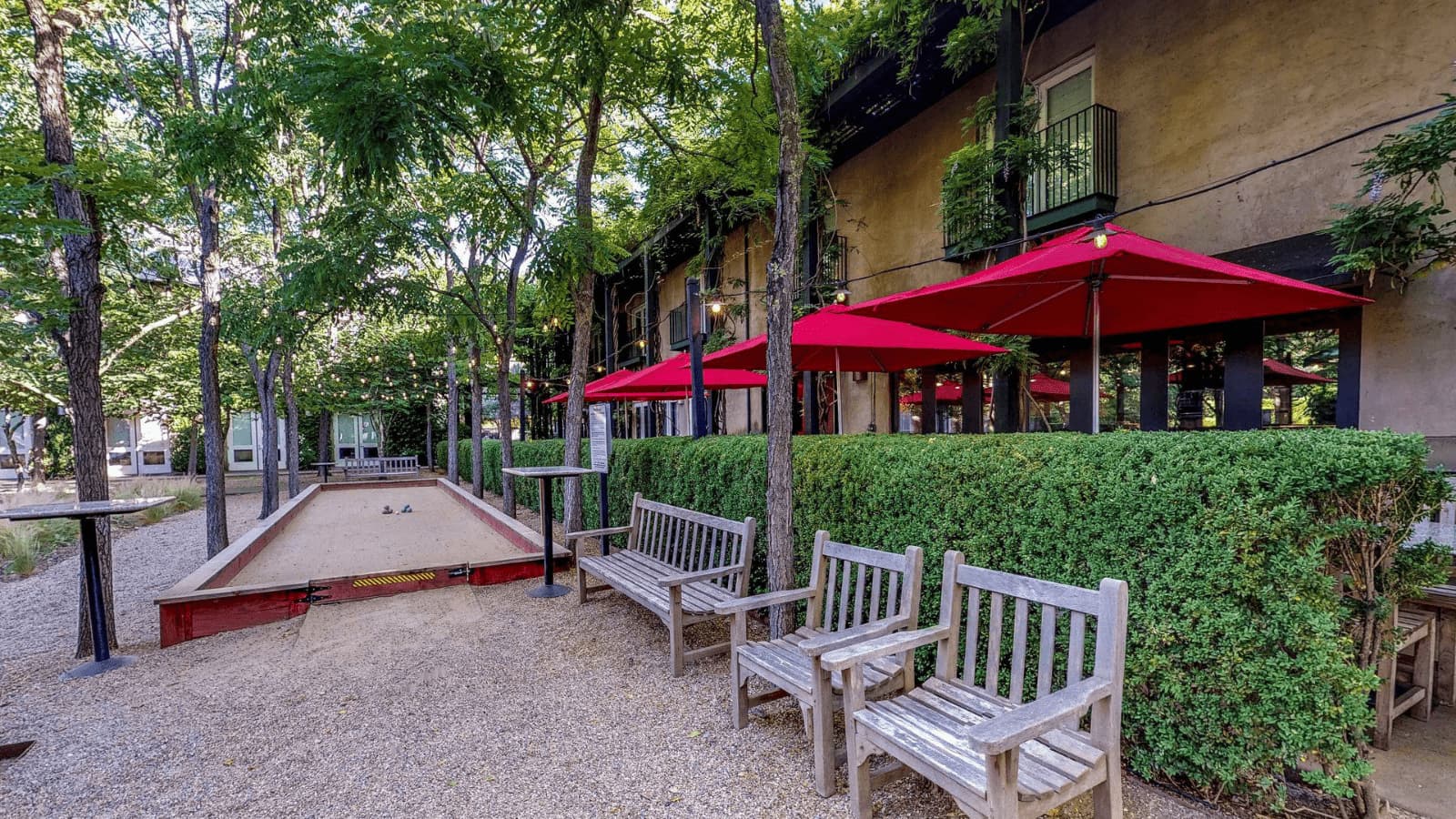 Outdoor seating with bocce court and red umbrellas.