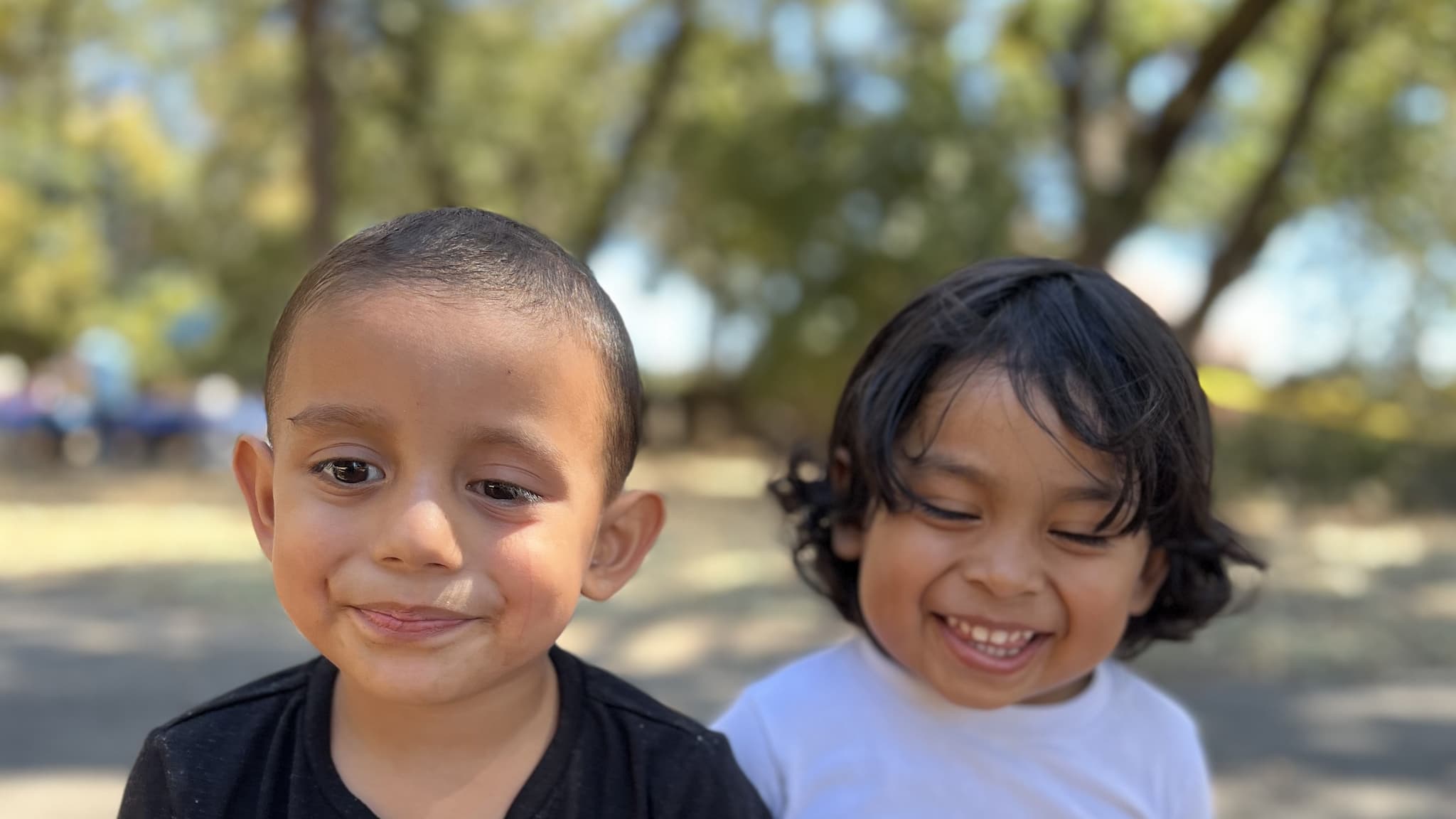 Two children smiling in a sunny park.