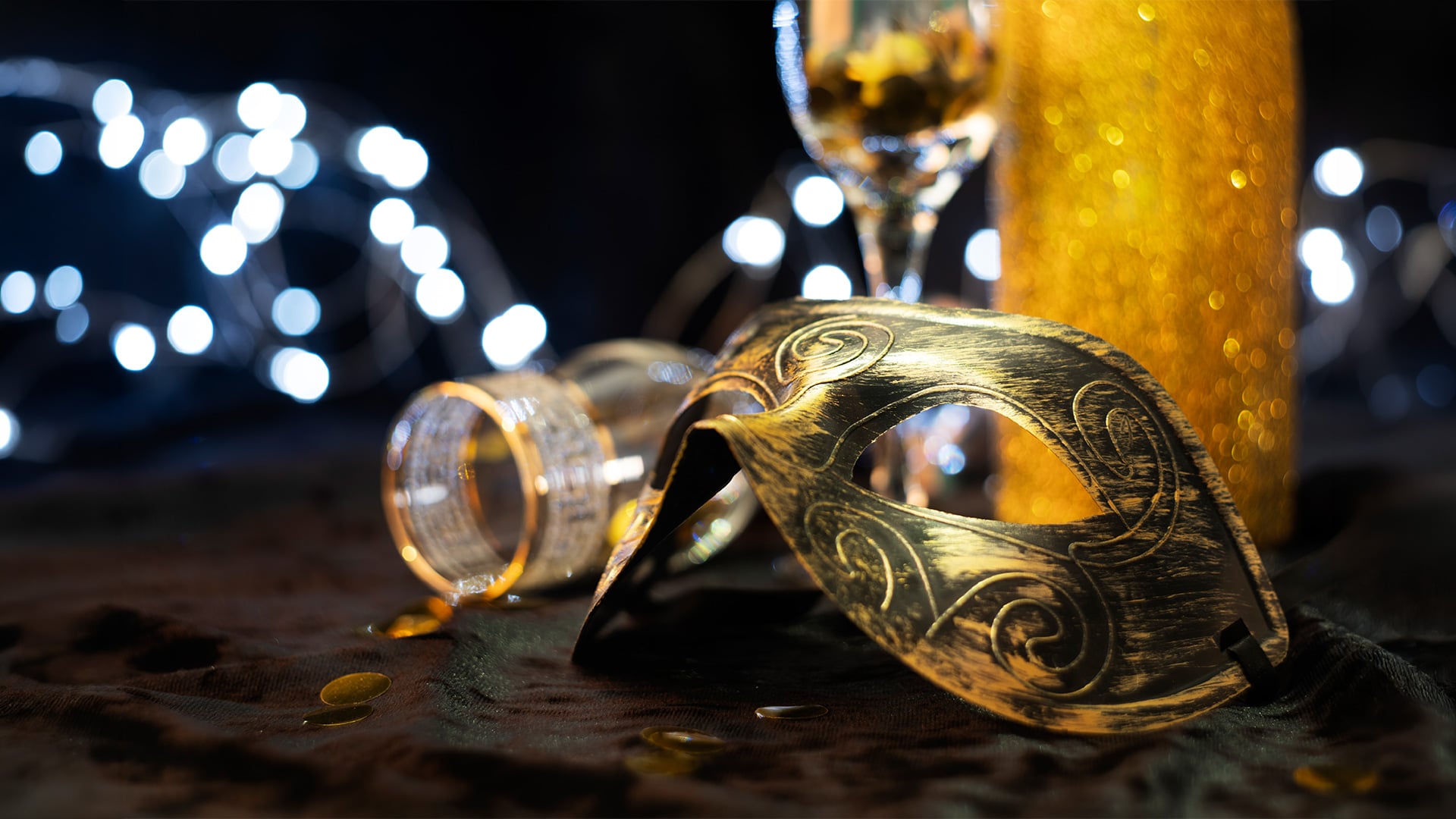 Gold Venetian mask beside champagne glass and glittering lights