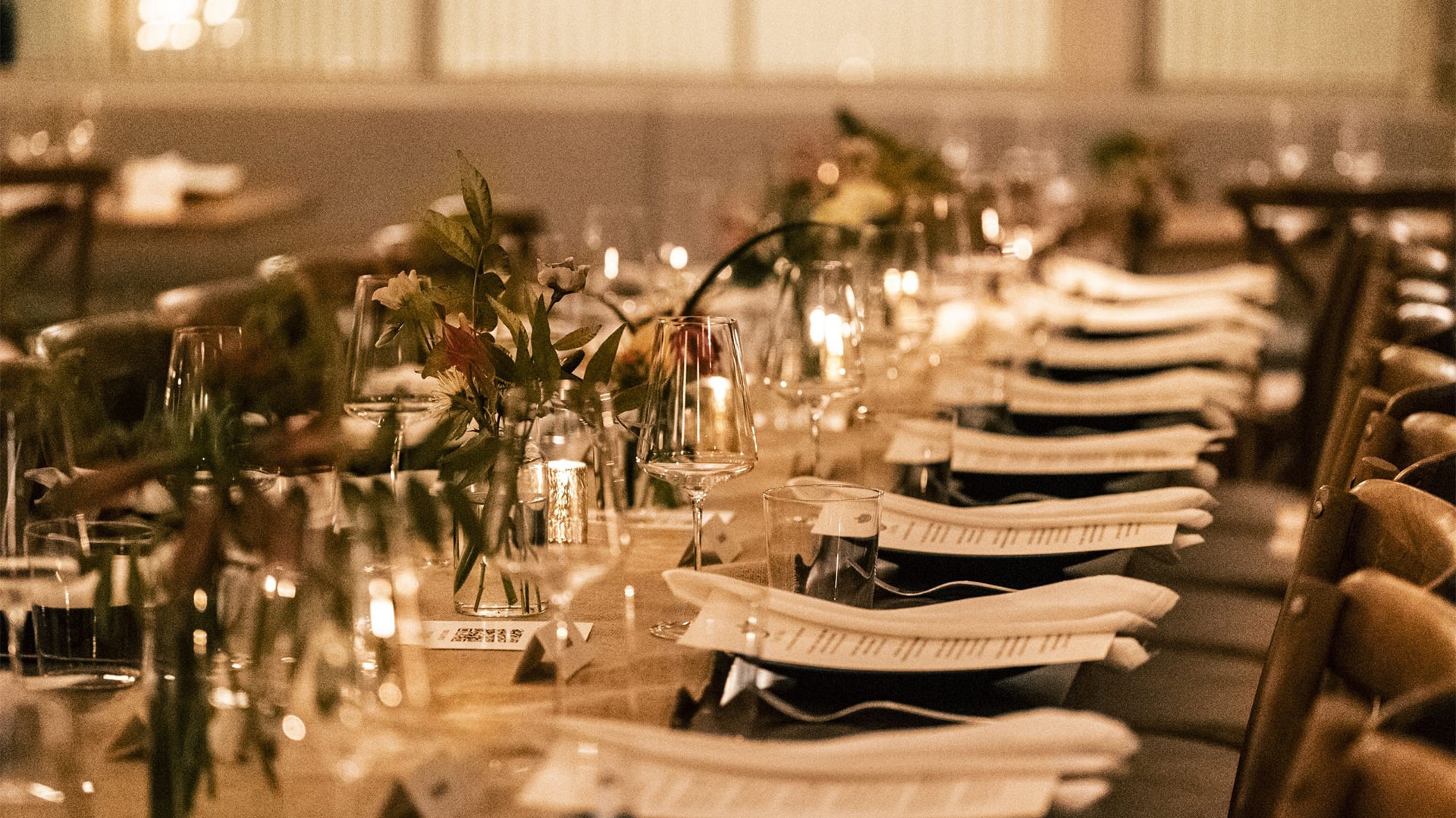 Warmly lit banquet table with flowers, glassware, and menus