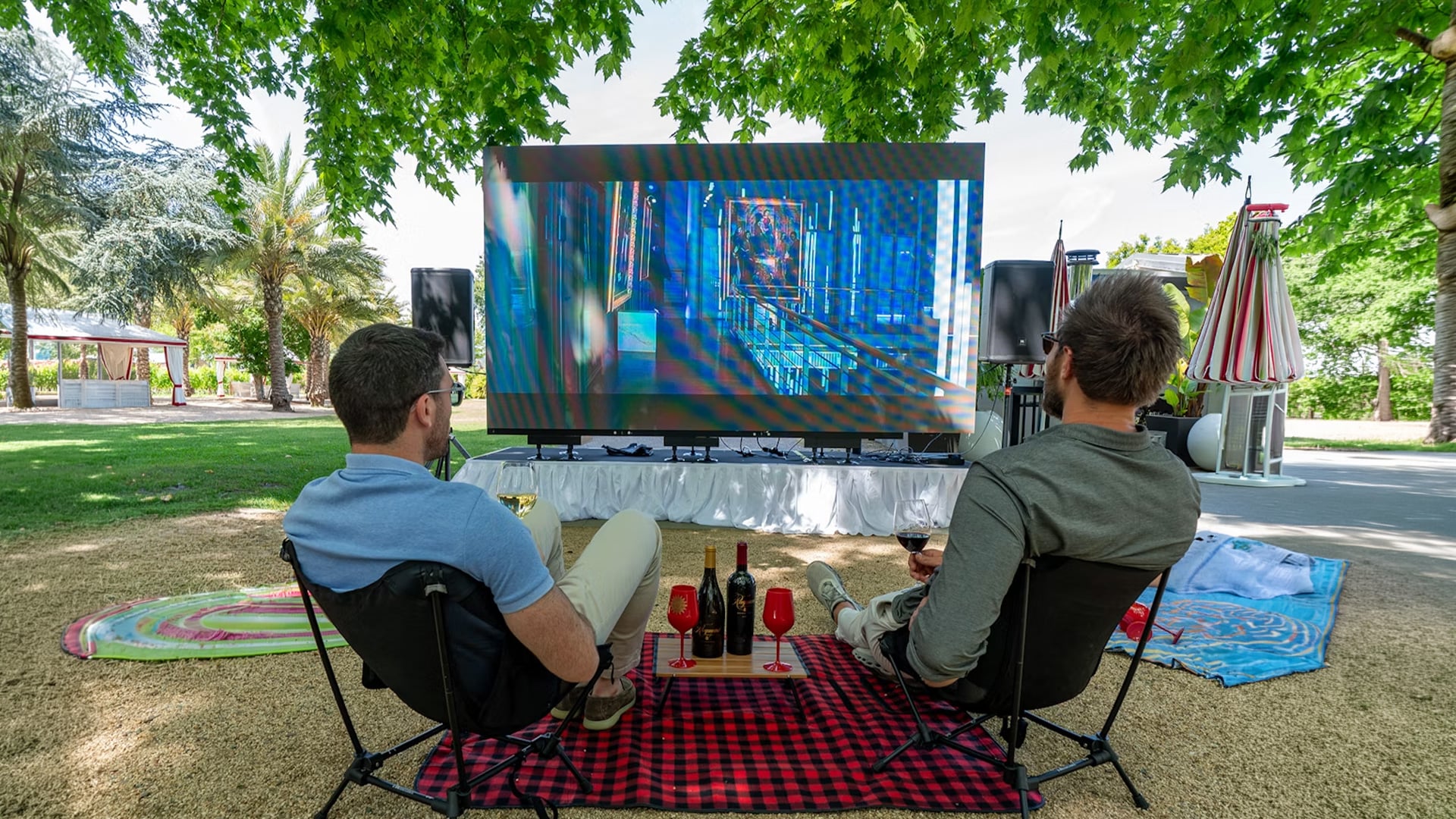 Two men watching outdoor movie with wine