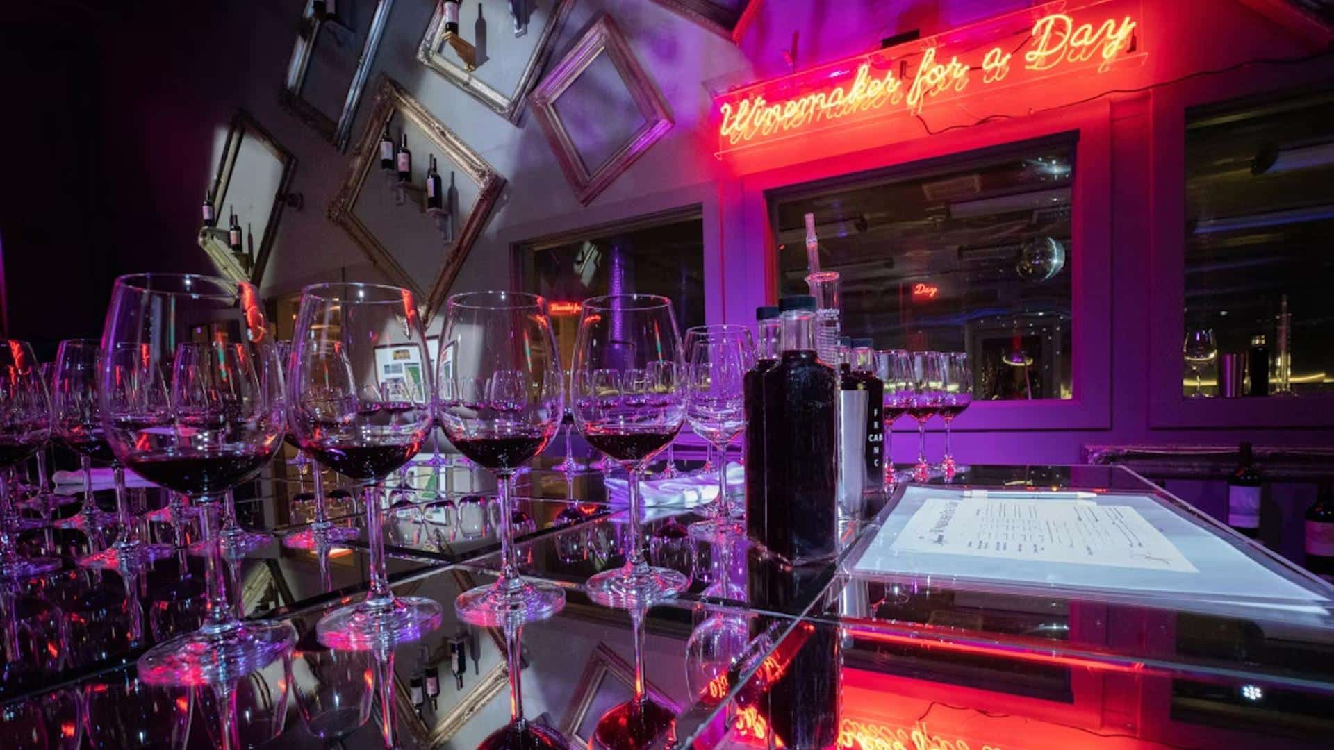 Wine glasses and neon sign in bar setting.