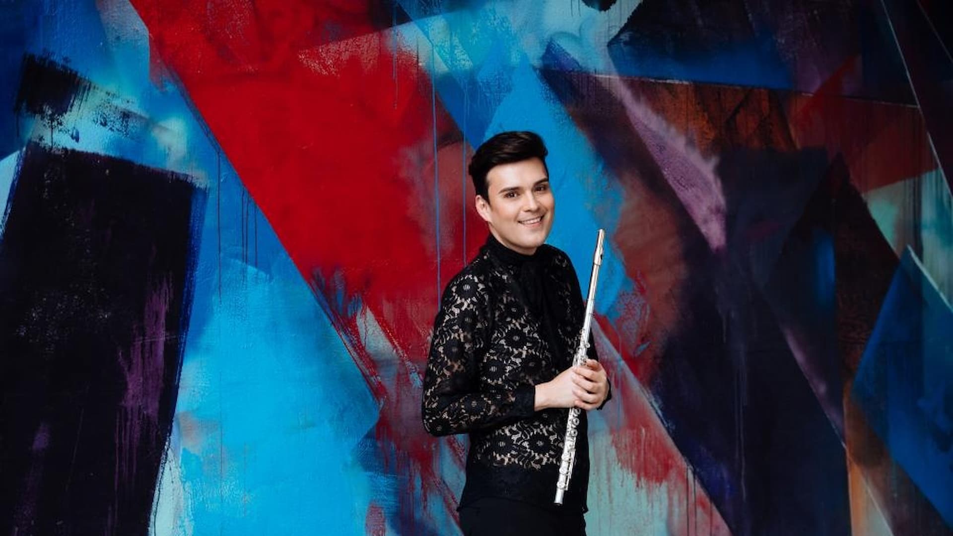 Person holding flute against colorful abstract wall.