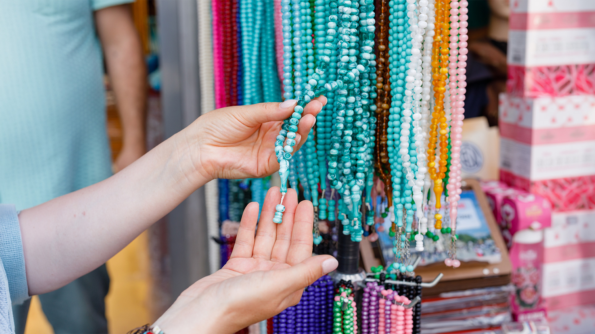 Hands examining turquoise prayer beads at a market stall