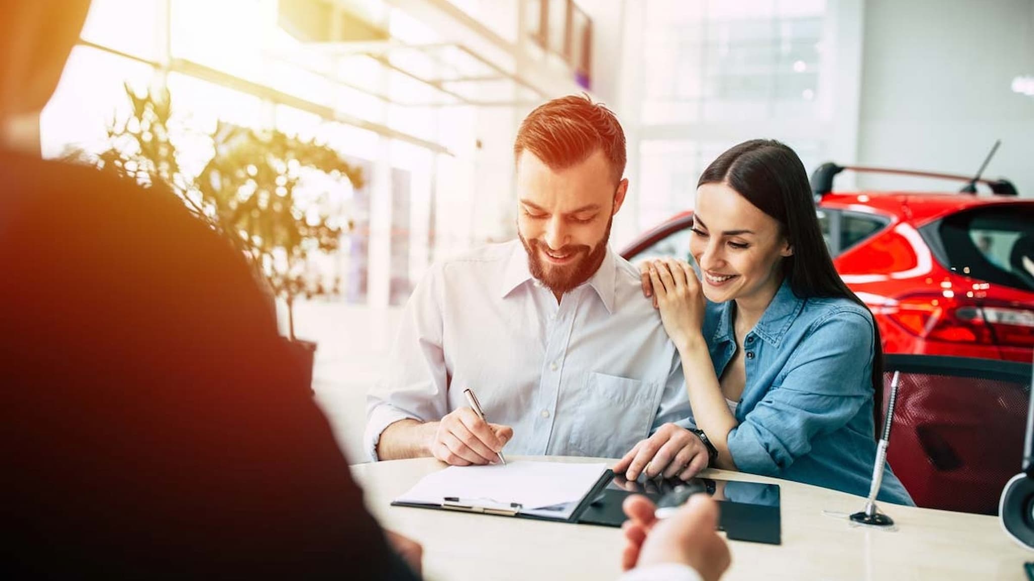 Couple signing car purchase agreement at dealership.