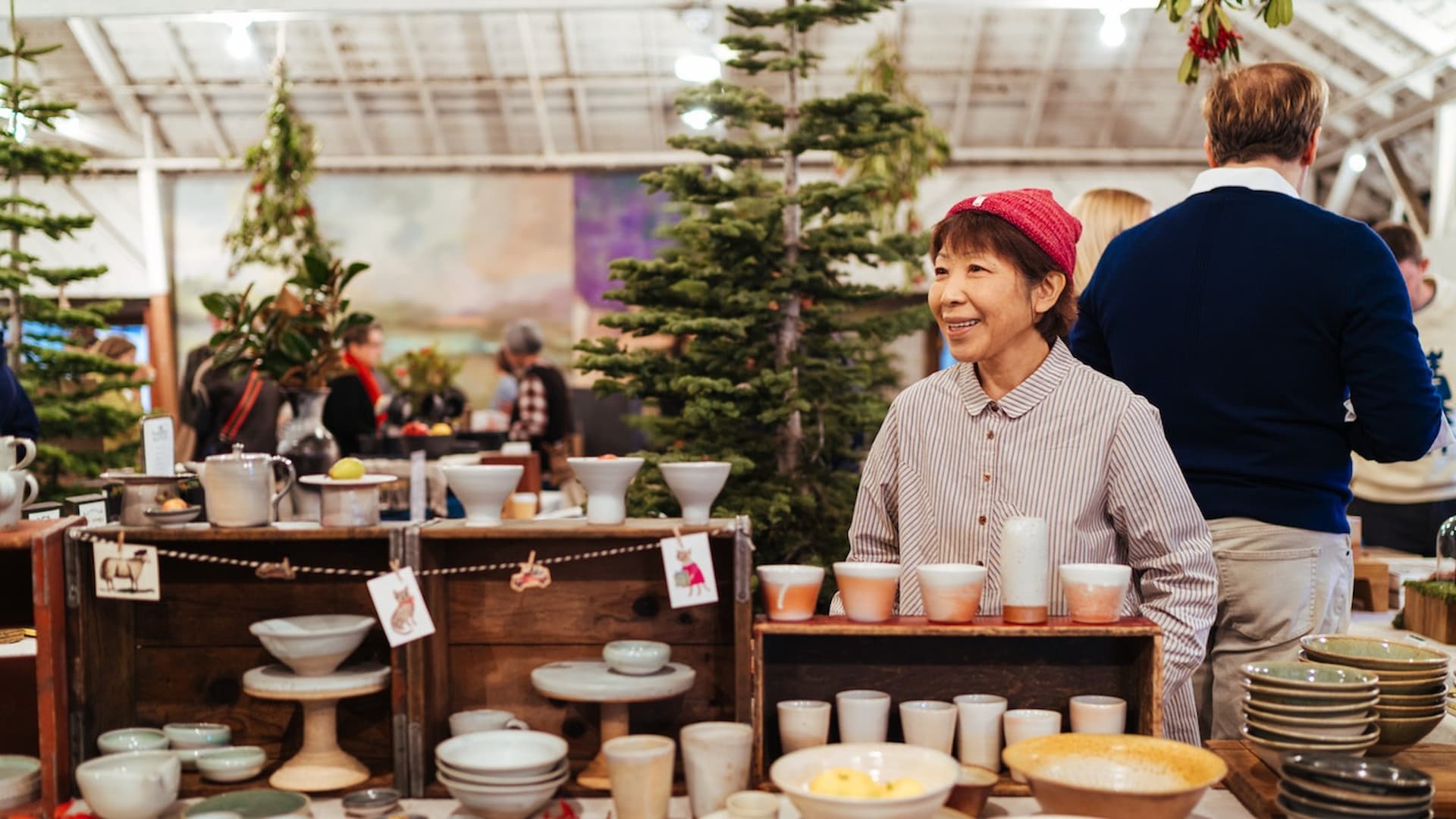 Woman selling pottery at festive market stall.