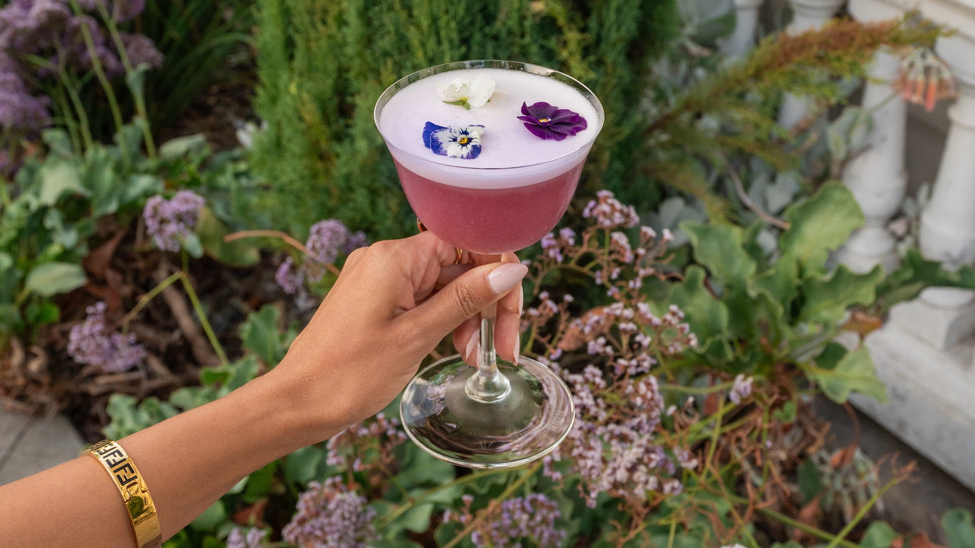 Hand holding floral-decorated cocktail in garden