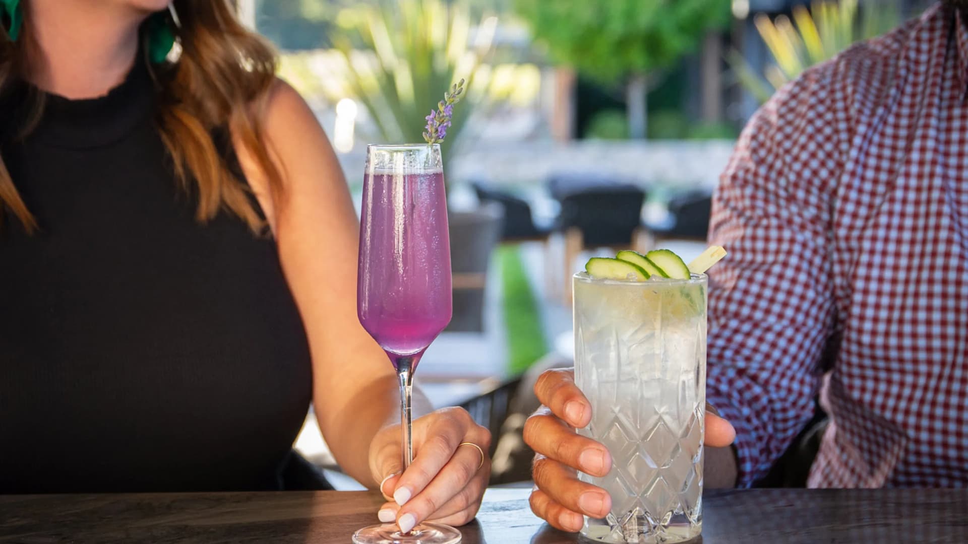 Two cocktails on table, people holding glasses.
