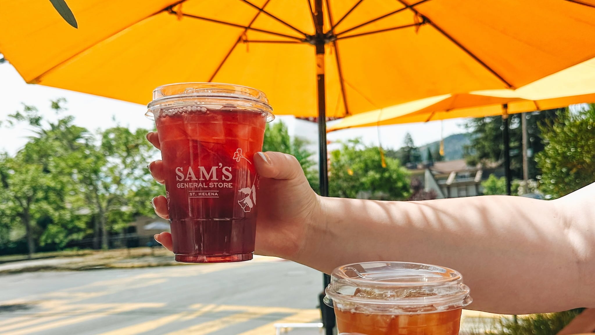 Hand holding red iced drink under yellow umbrellas