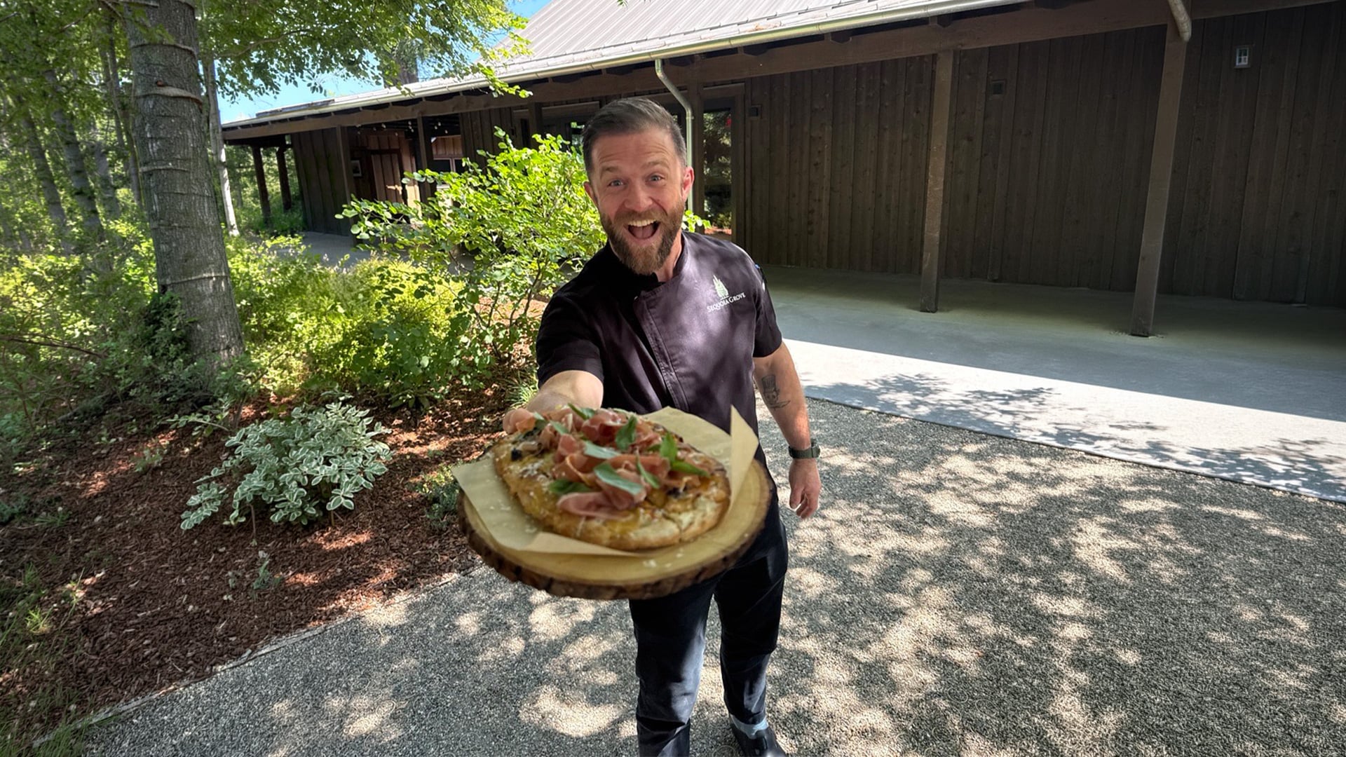 Chef holding pizza outdoors near wooden building
