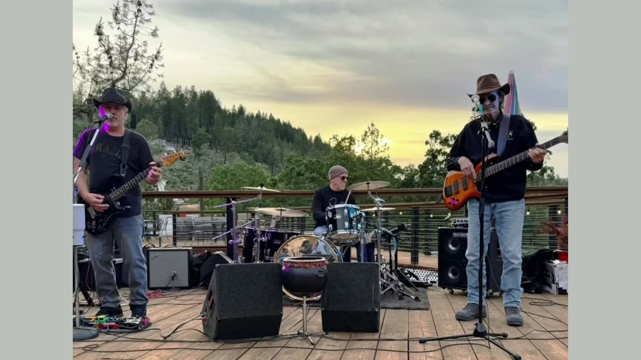 Three musicians performing on outdoor deck at sunset