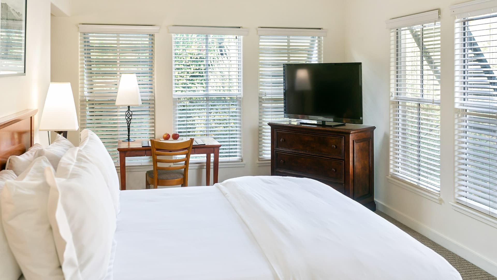 Bright bedroom with bed, TV, and desk.