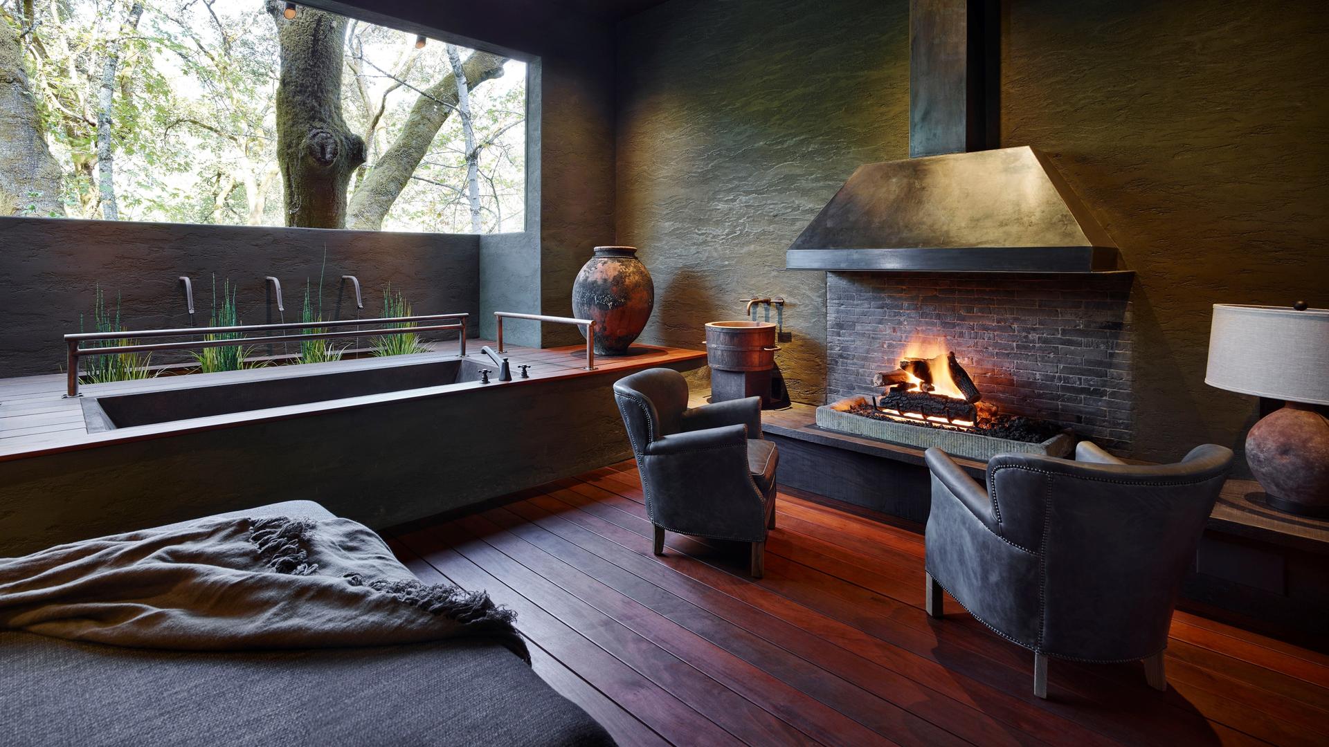 Cozy fireplace with chairs and bathtub beside window.