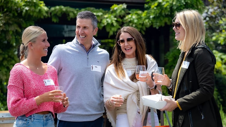 Four people laughing and holding drinks outside.