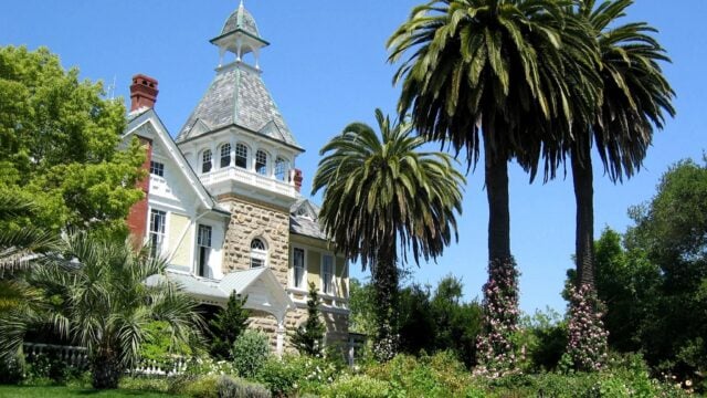 Victorian mansion surrounded by palm trees and garden.