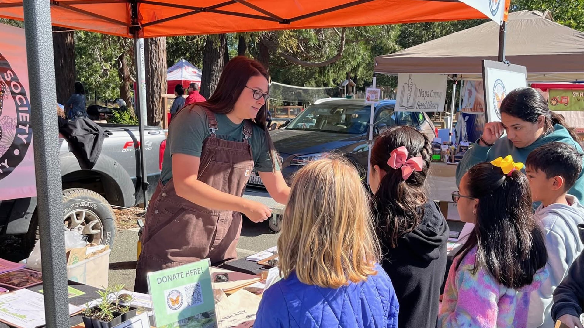 Woman speaking to children at outdoor market booth