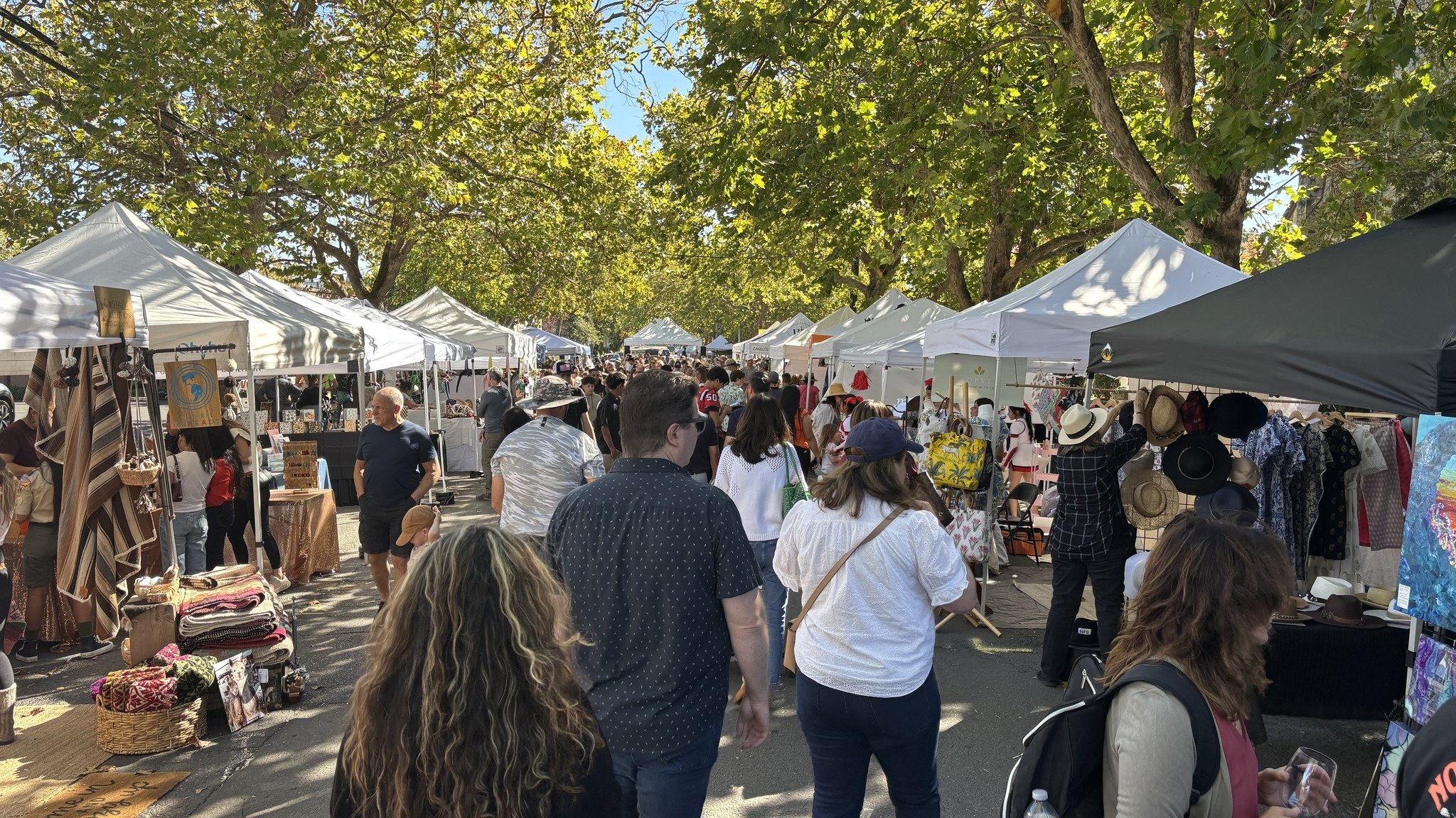 Crowded outdoor market with tents and shoppers.
