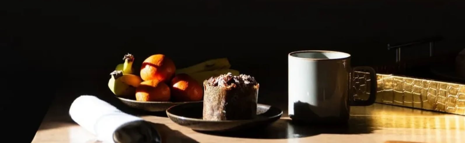 Sunlit breakfast table with muffin, fruit, and mug