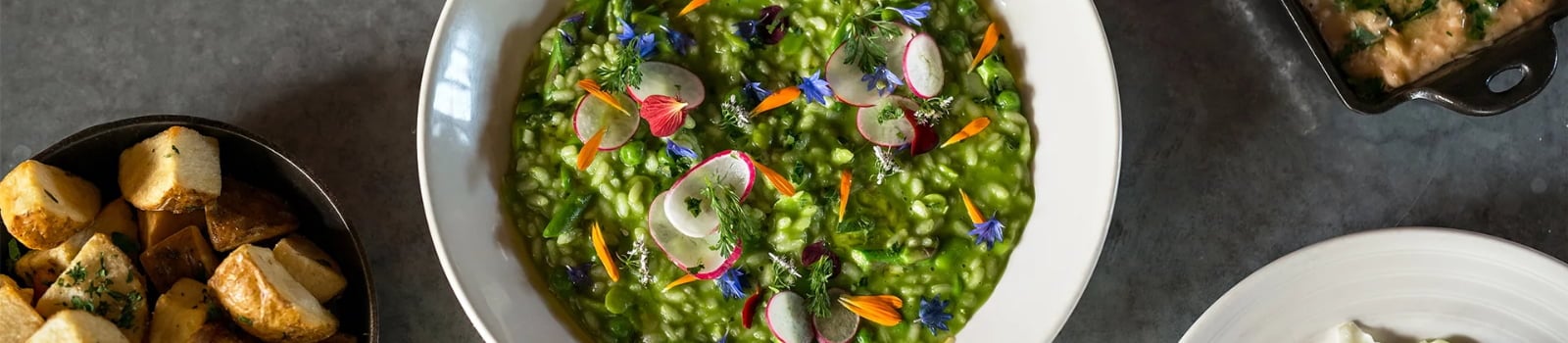 Green risotto topped with radishes, herbs, and edible flowers